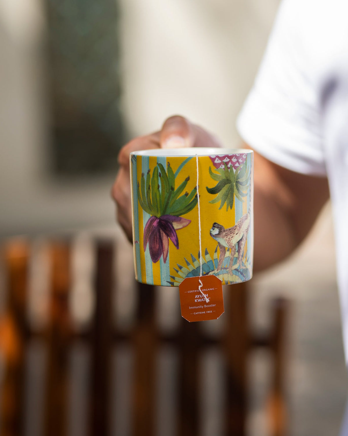 Person holding a yellow Mahi Mug with a tea bag tag hanging below.