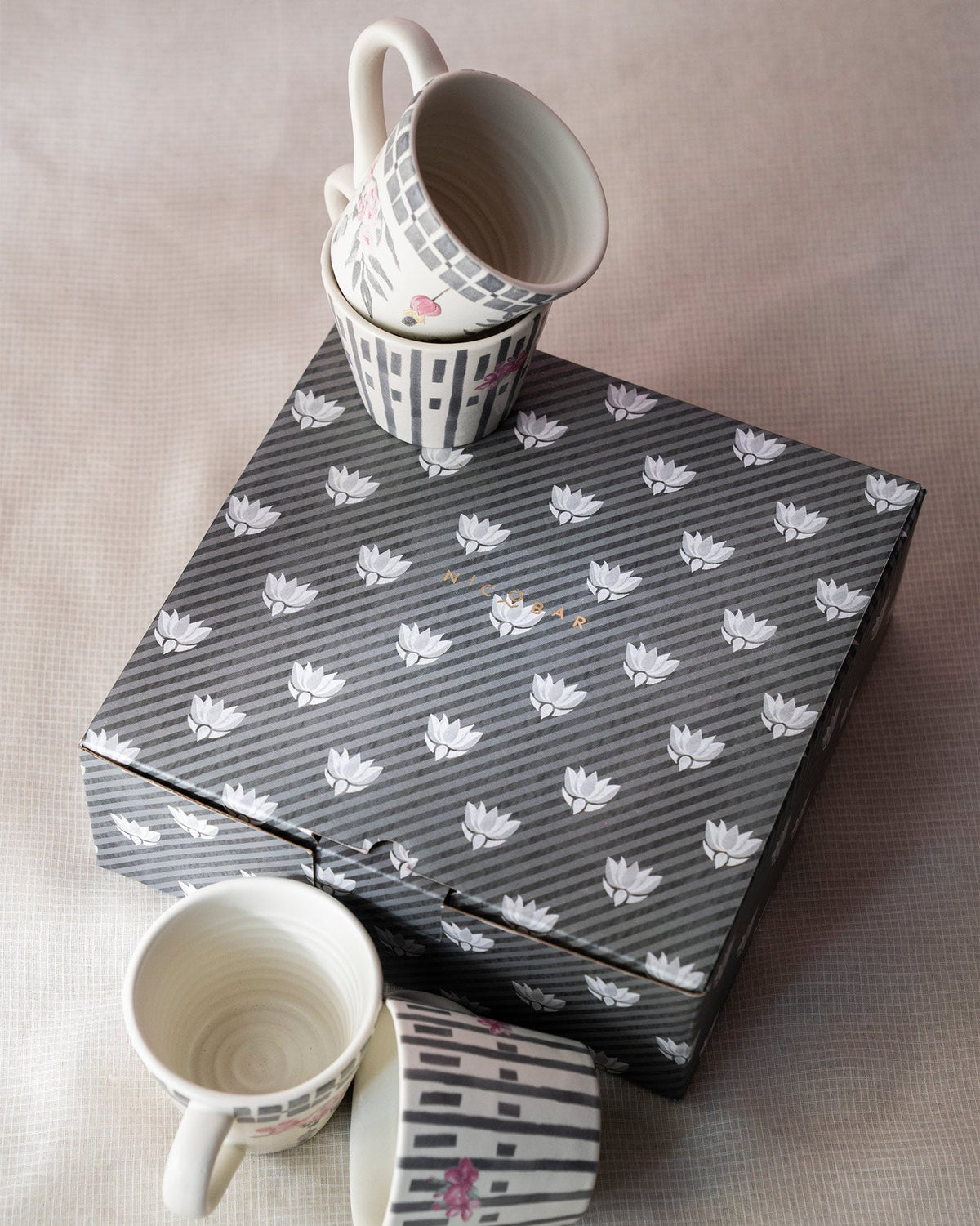 Set of four Nectar espresso mugs with pink florals beside a striped lotus gift box.