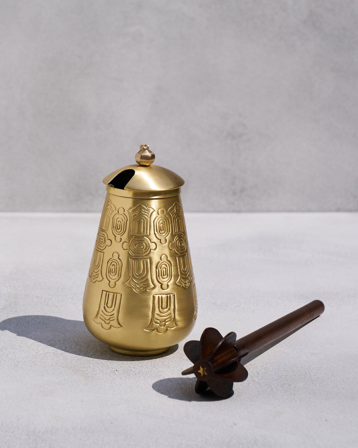 Matte gold embossed Dariya lota with lid beside a dark wood star-head churner.