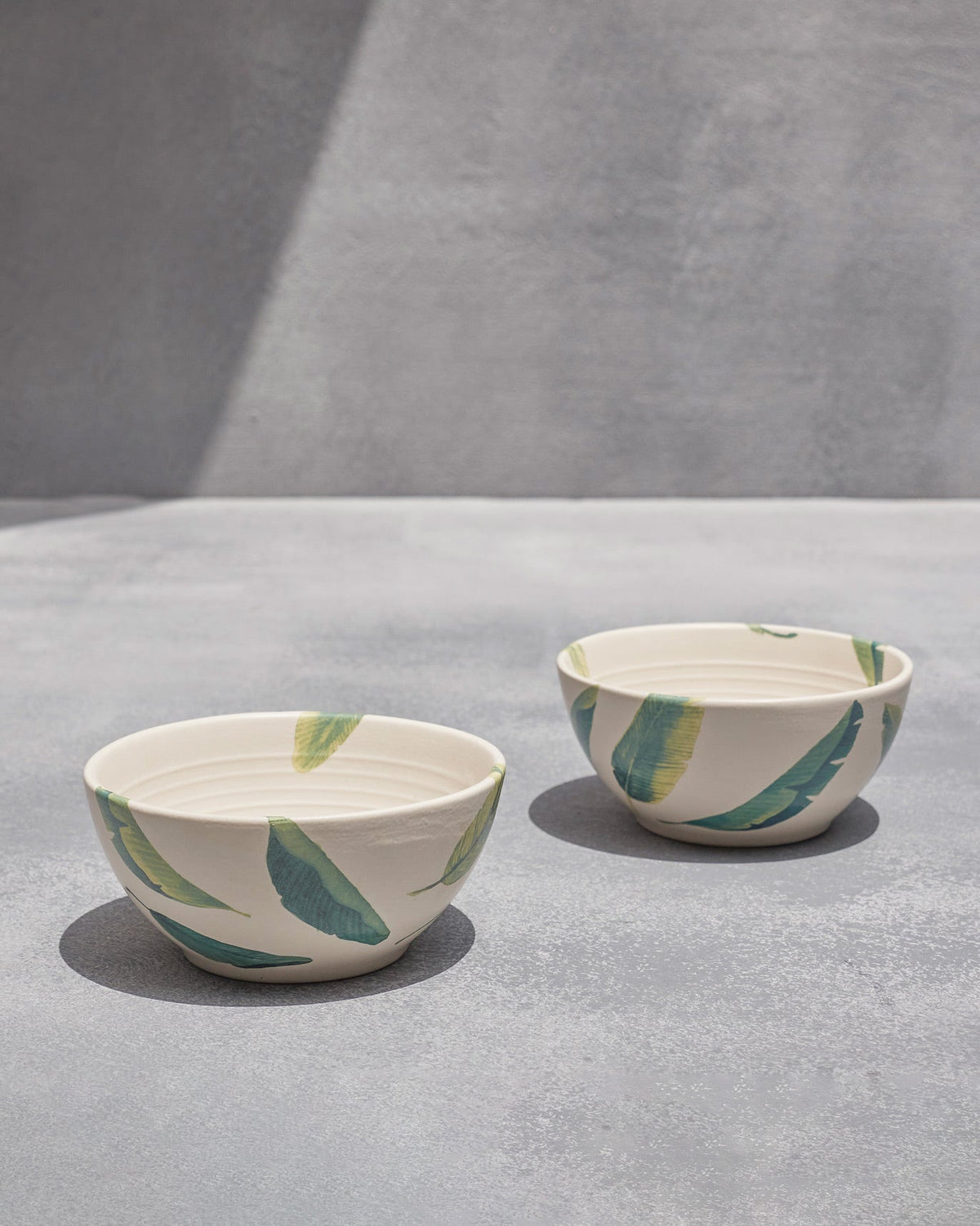 Pair of Ceylon cereal bowls with green banana-leaf motifs on cream stoneware.