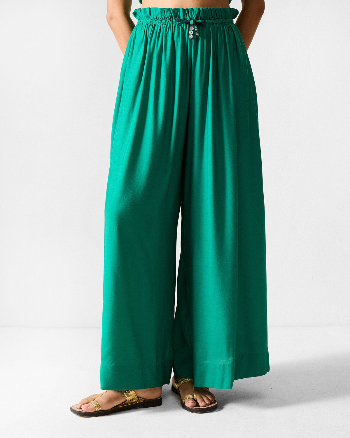 Person wearing green paperbag pants with a gathered waist and wide legs.