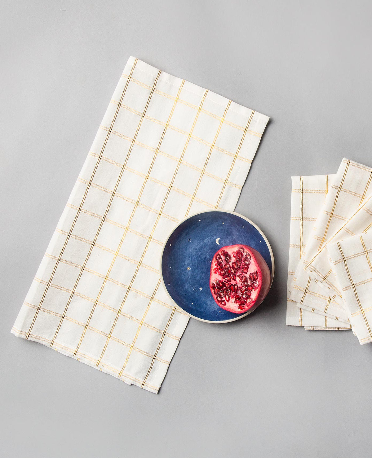 Cha Napkin laid flat on a grey surface, with a plate and a folded stack beside it.