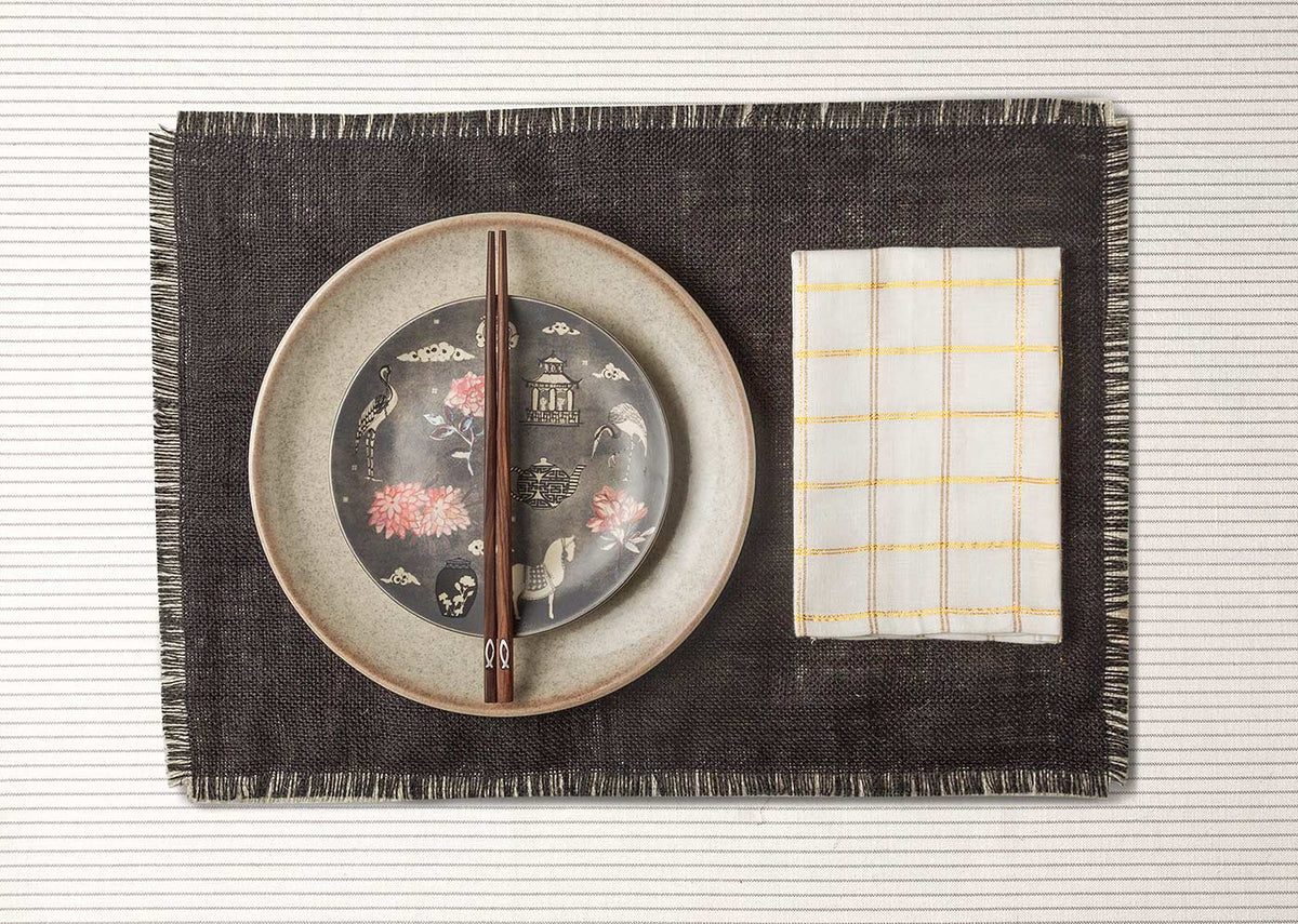 Cha Napkin on a dark placemat beside a patterned plate.