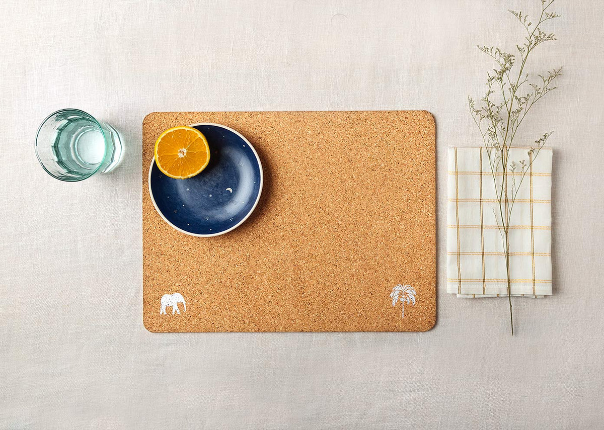 Cork placemat with white elephant and palm motifs on a laid table.