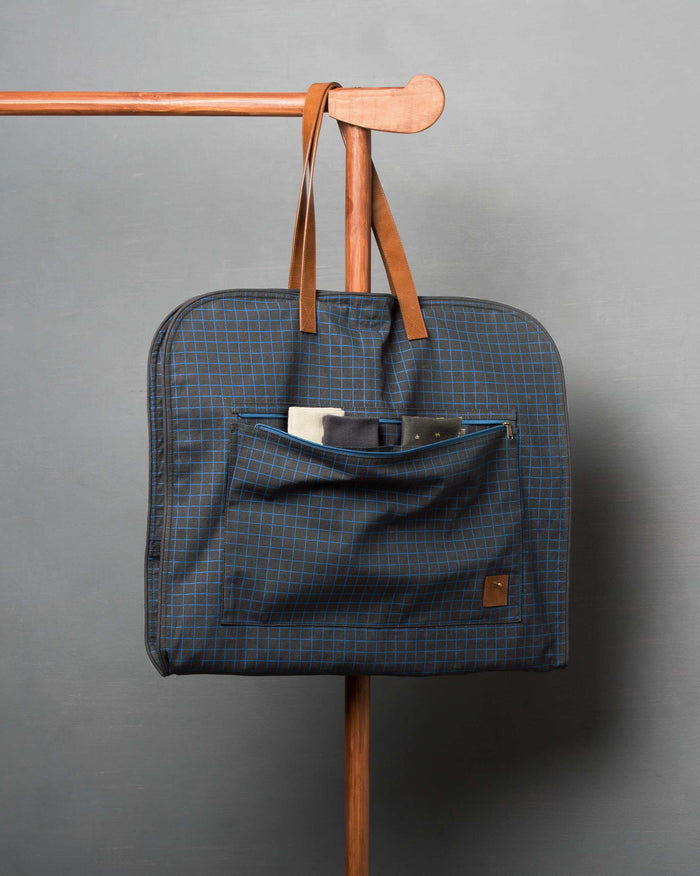 Front of the Hanging Coat Bag hung from a wooden rail by tan leather handles.