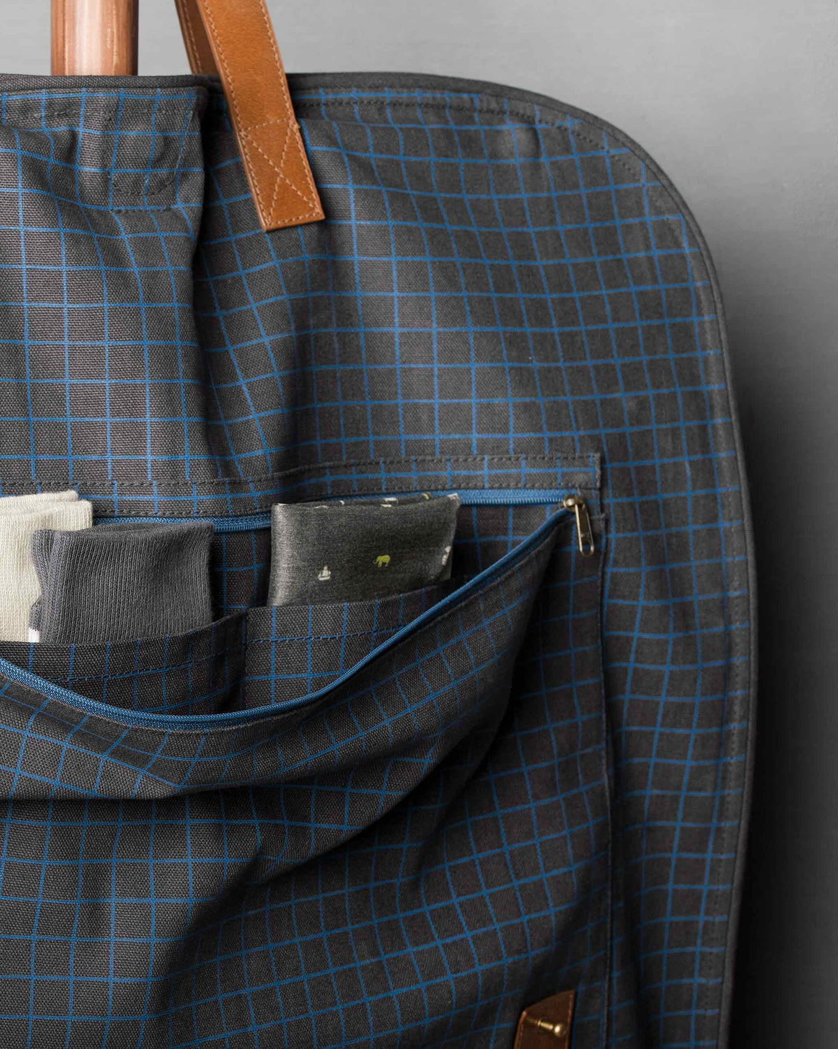 Close-up of the Hanging Coat Bag front pocket, with a zip and navy check fabric.