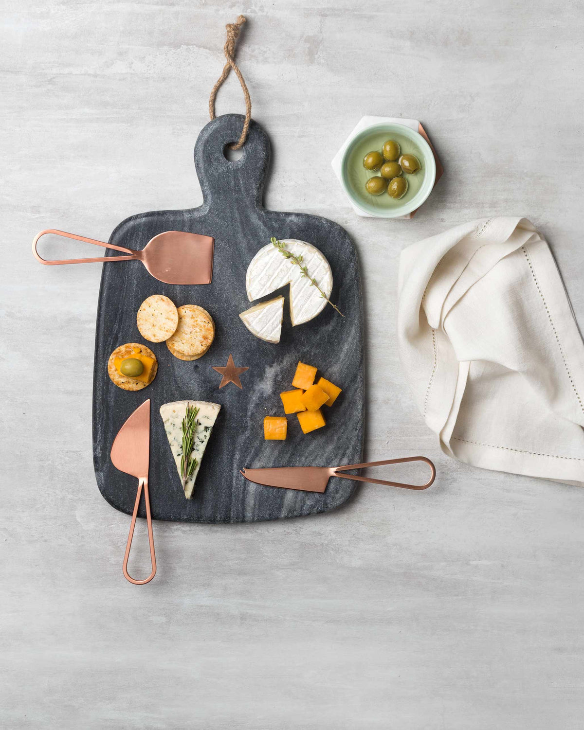 Overhead view of Cheese Knives used on a grey board with crackers and cheese.