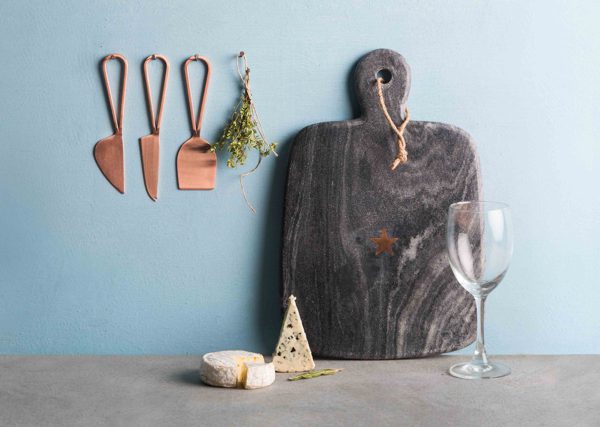Set of three Cheese Knives hanging beside a grey serving board.
