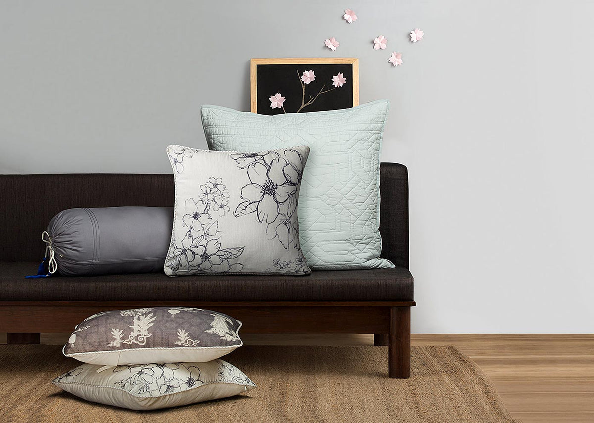 Sakura Cushion Cover on a dark sofa beside other cushions.