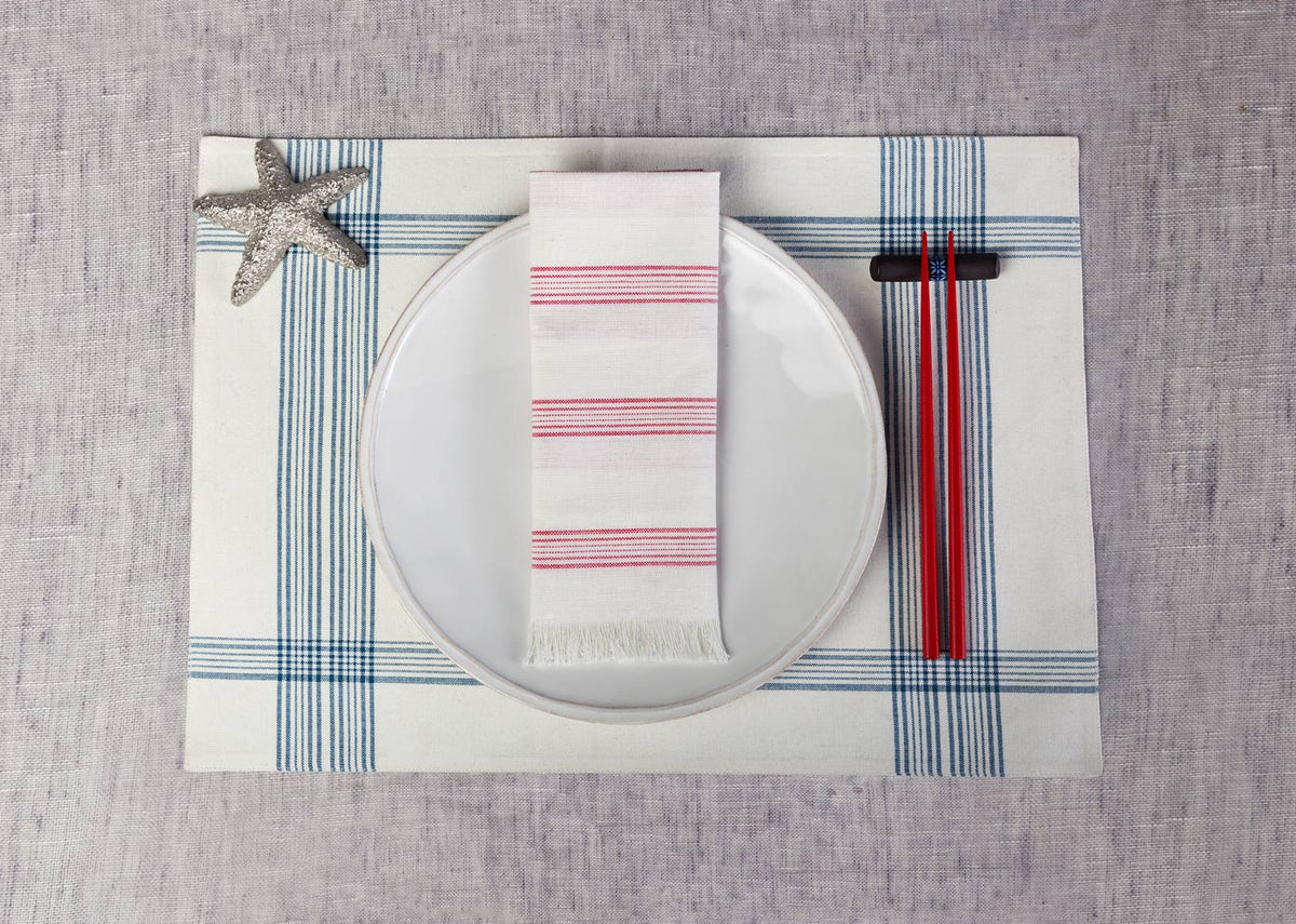 Shima Dinner Napkin in ivory with red stripes folded on a white plate.
