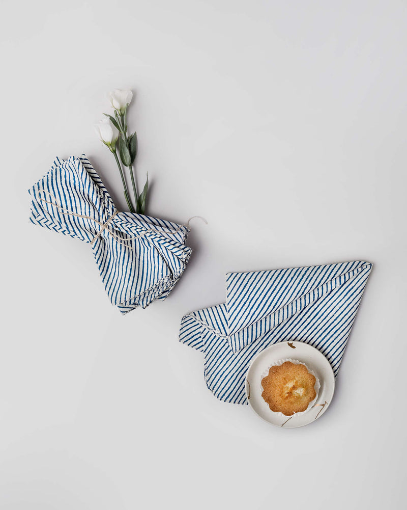 Aozora Stripe Dinner Napkins in dark blue, one folded beside a small plate.