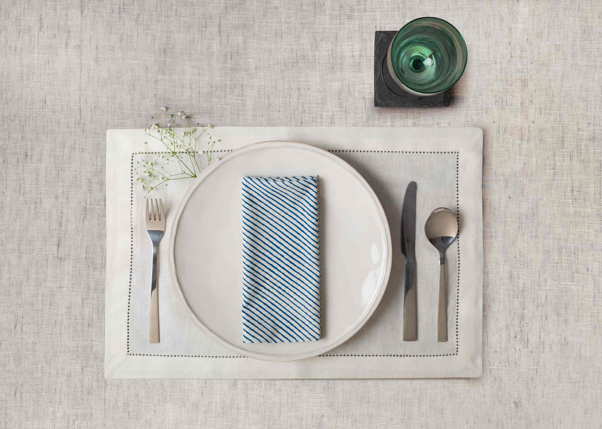 Aozora Stripe Dinner Napkin in dark blue, folded on a plate in a place setting.