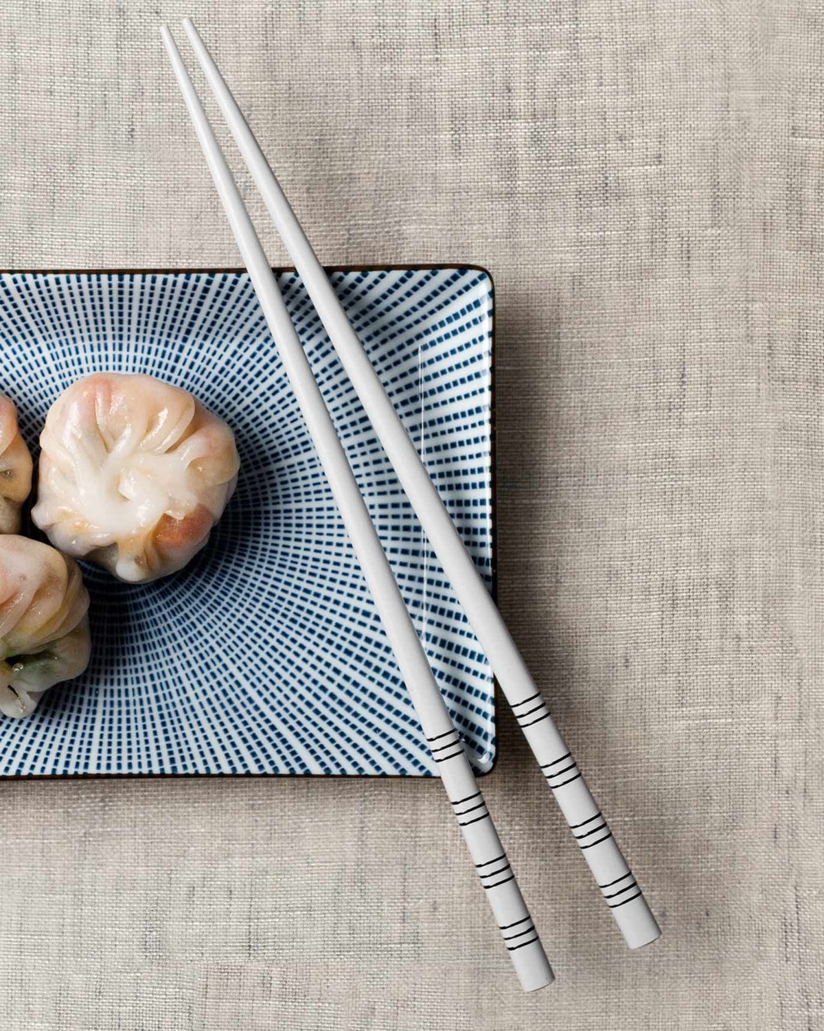 Stripe White Chopsticks resting on a blue dotted plate with dumplings.