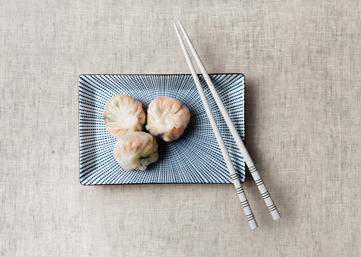 Stripe White Chopsticks set at an angle across a blue dotted plate with three dumplings.