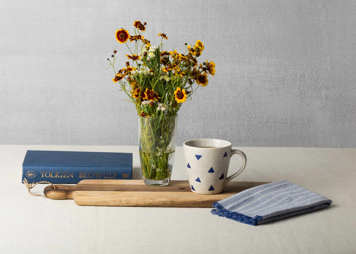 Sencha mug on a wooden board beside a vase of flowers.