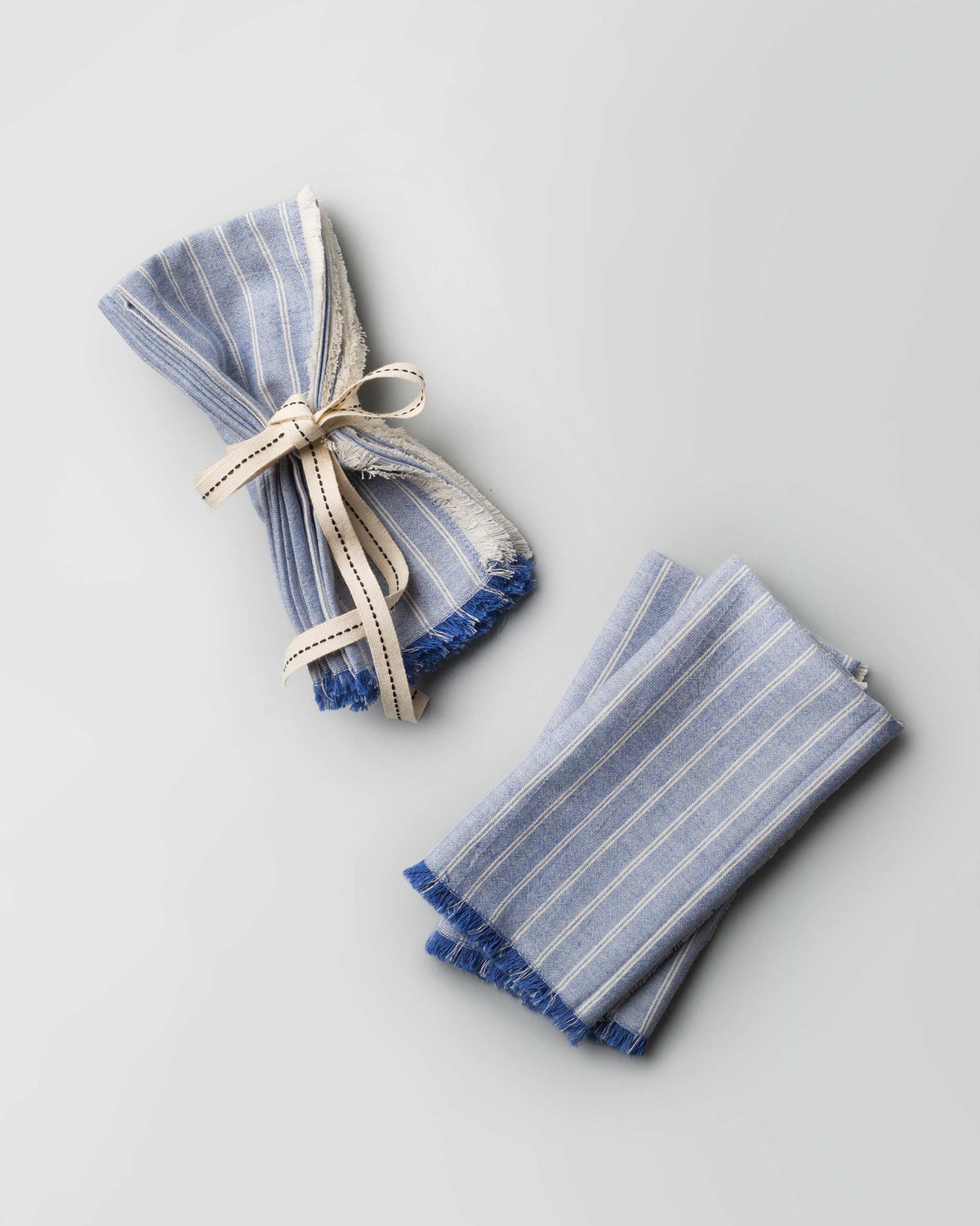Daburu Stripe Dinner Napkins in blue, one bundled with a cream ribbon.