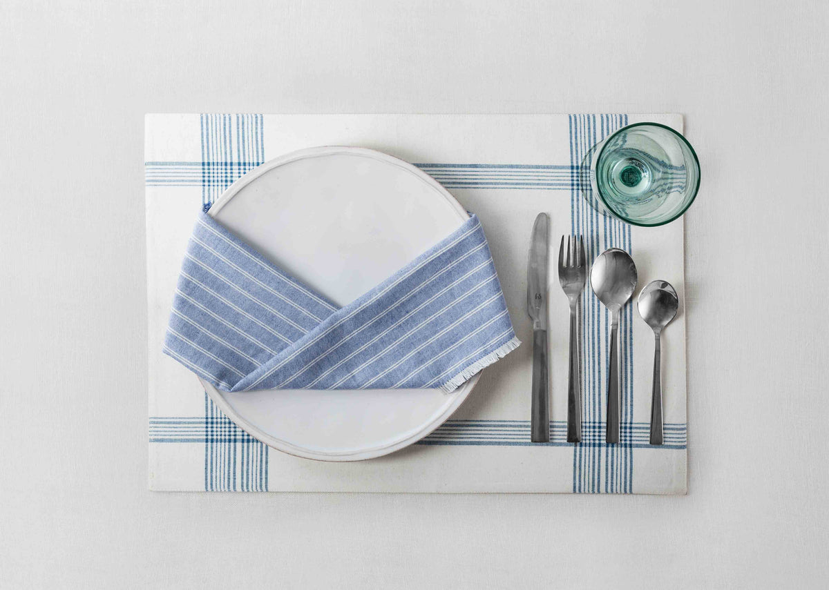 Daburu Stripe Dinner Napkins in blue, folded on a white plate.