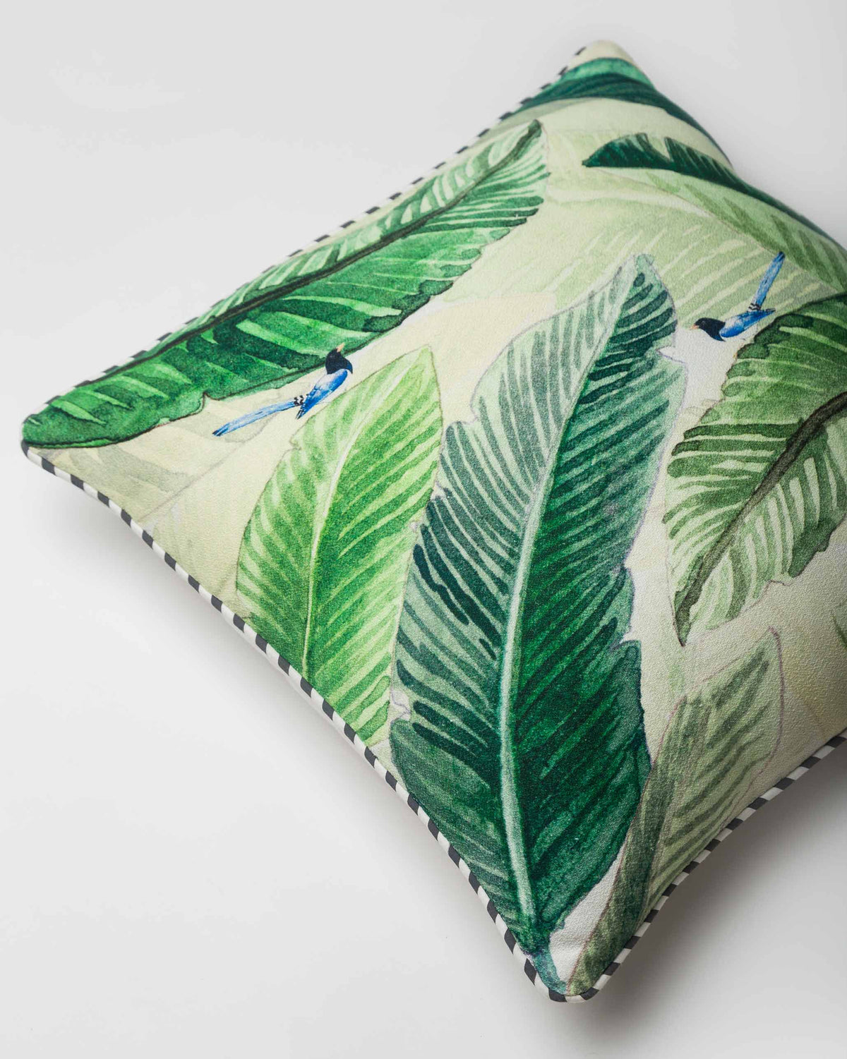 Angled view of the Banana Leaf Cushion Cover with striped piping along its edge.