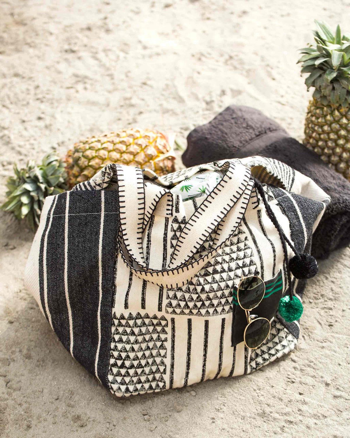 Coast Bag resting on sand, showing its black and cream triangle weave.