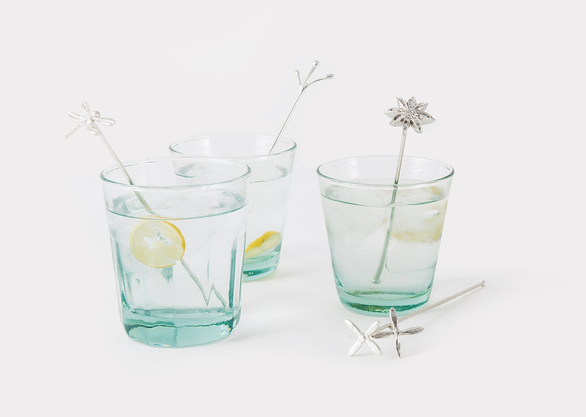 Stirrers in two glasses of water, with a silver stirrer lying beside them.