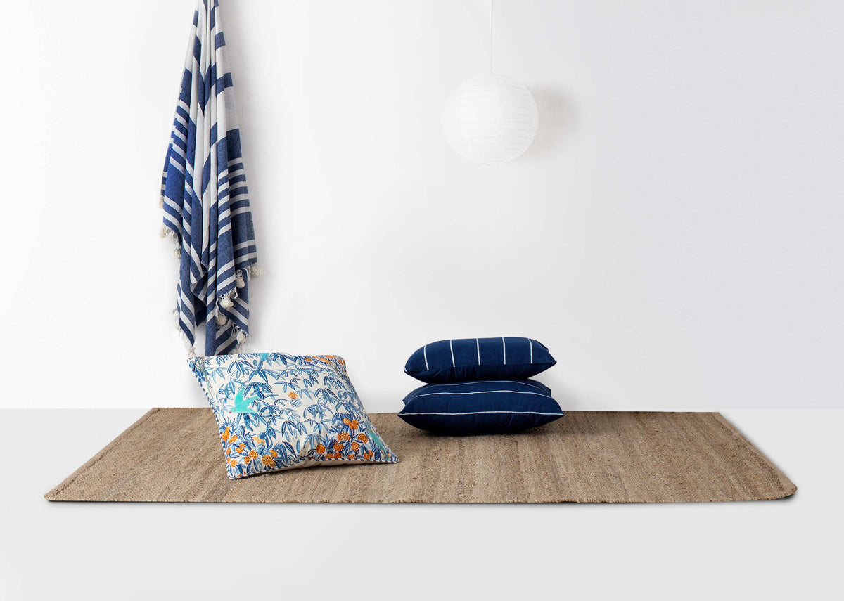 Kumarakom Flora cushion cover on a jute rug beside navy cushions.