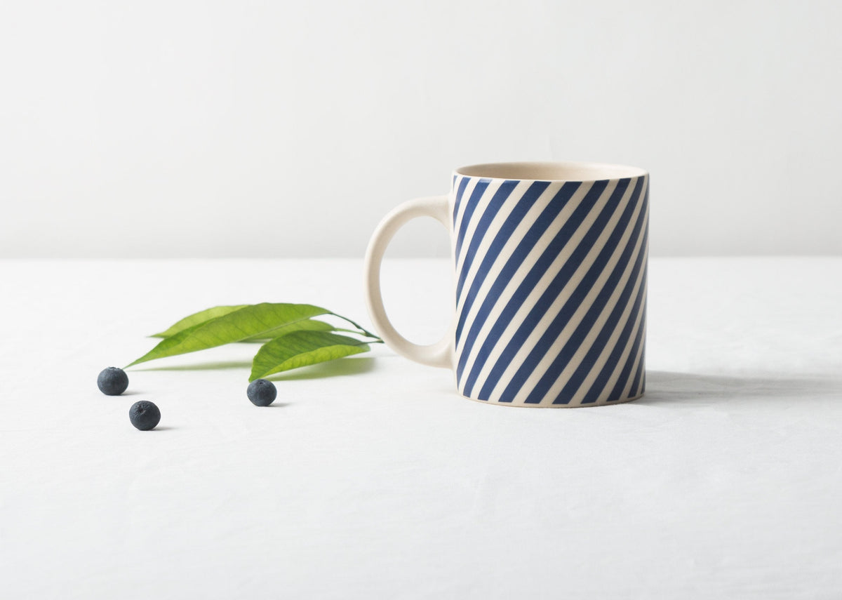 Kumarakom candy stripe mug on a table beside blueberries and leaves.