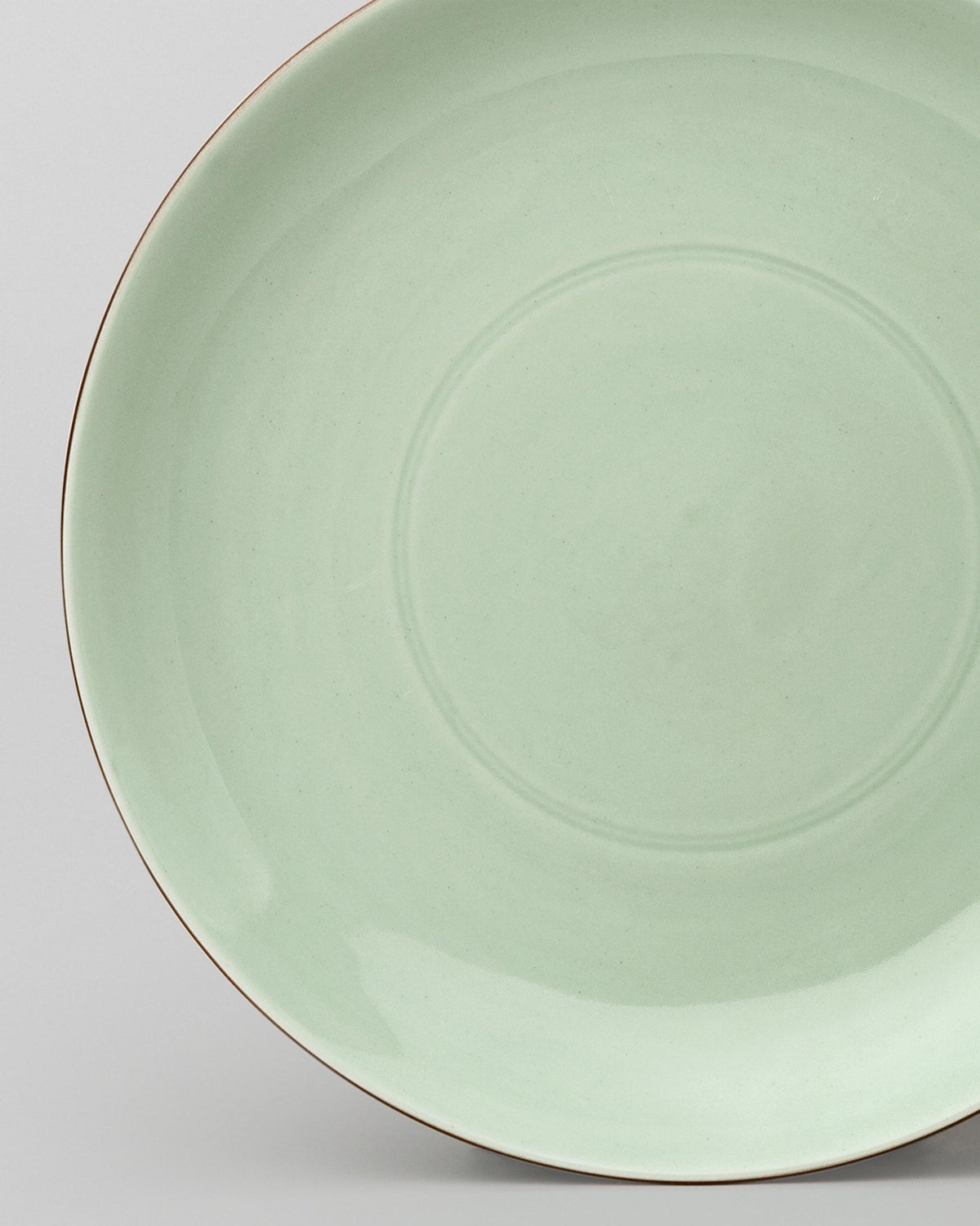 Close-up of a Celadon Dinner Plate showing its glaze and thin brown rim.