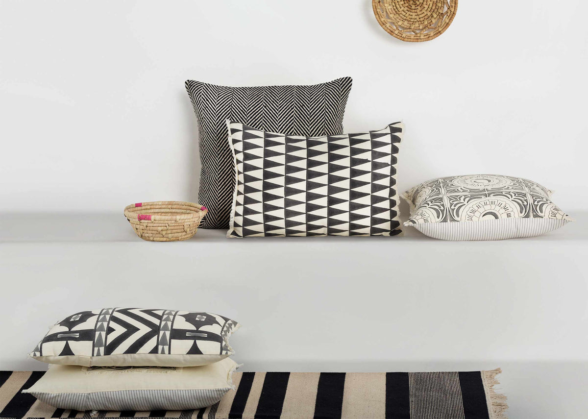 Giza Pillow Cover among other cushions on a white shelf.