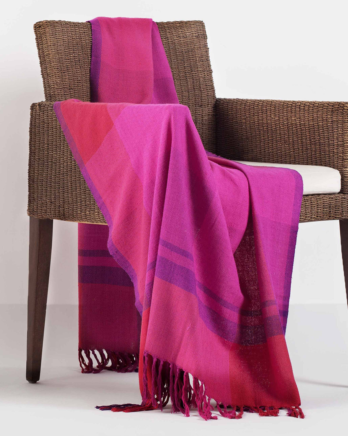 Tangier Handloom Throw in fuchsia draped over a wicker chair.