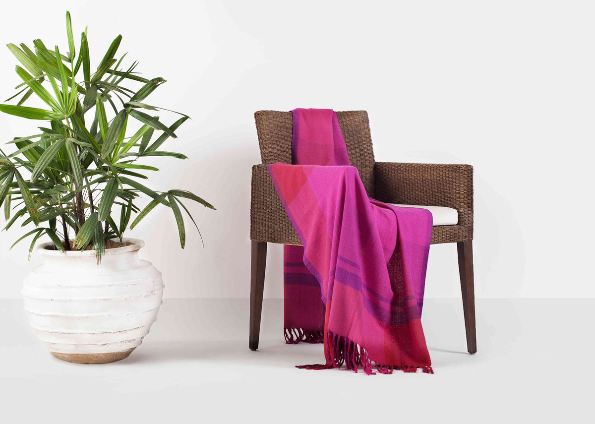 Tangier Handloom Throw in fuchsia hung over the arm of a wicker chair.