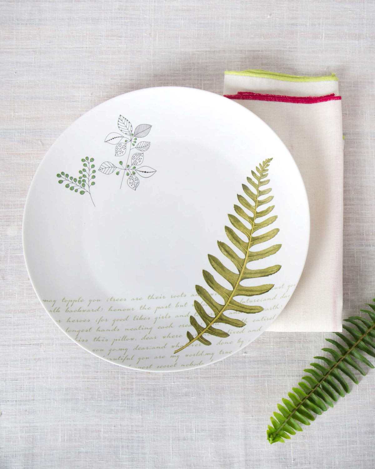 Flora Fauna Dinner Plate with a fern and leafy sprigs, seen from above.