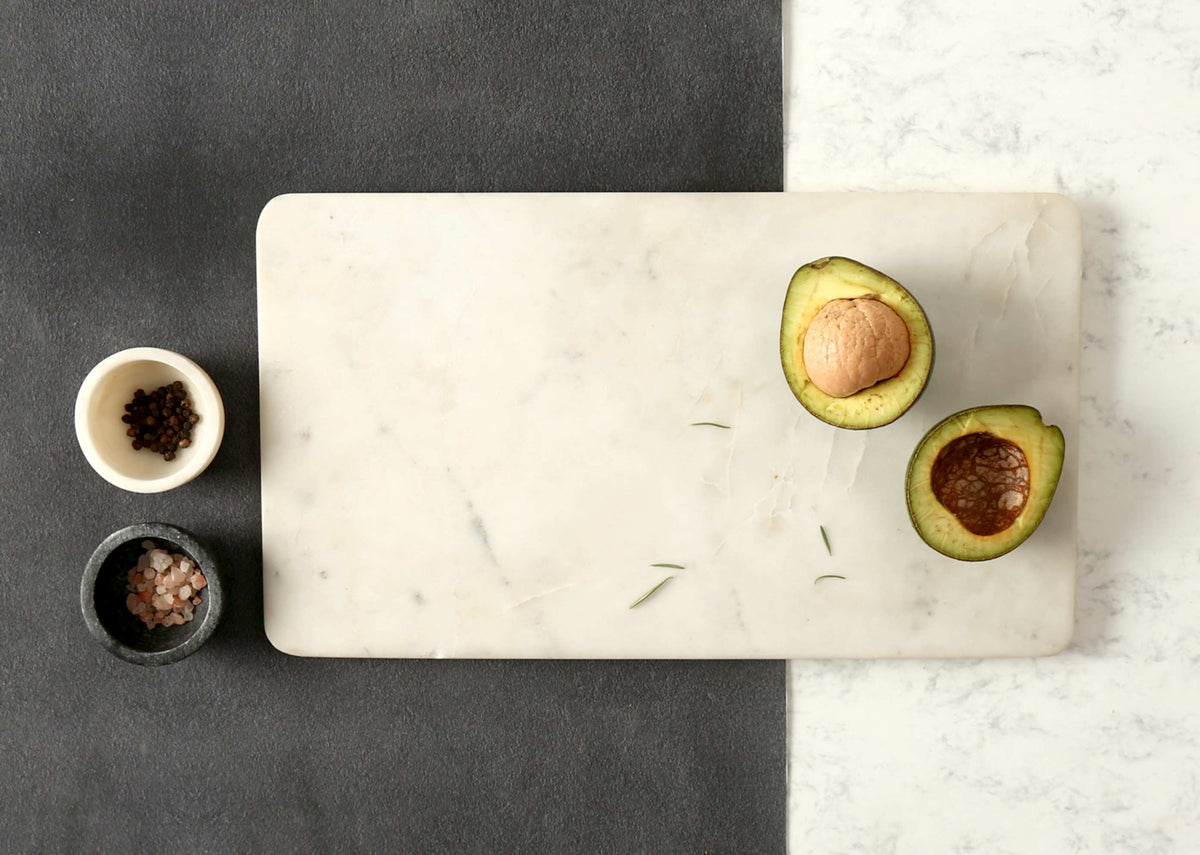 Marble Cheese Board with two halved avocados and small salt bowls.