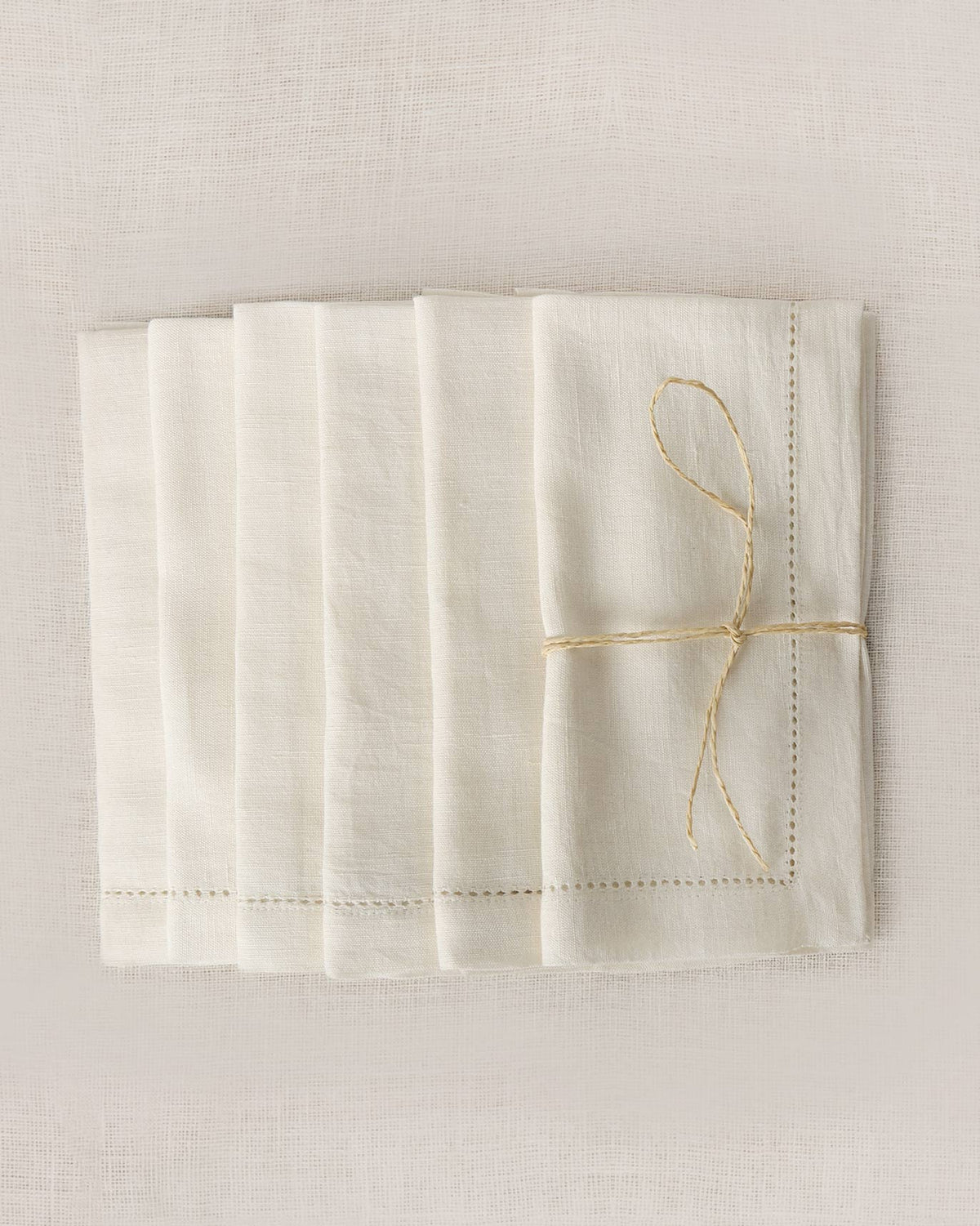 Ivory Verandah dinner napkins stacked and tied with string, with a stitched border.