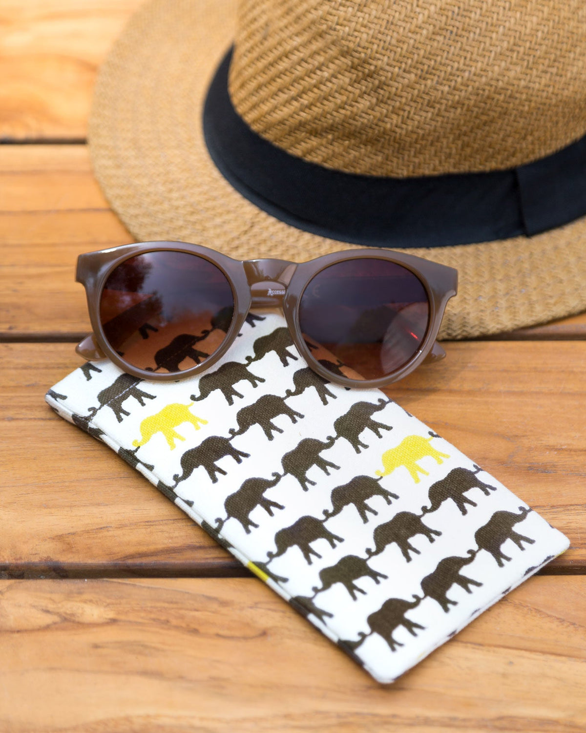 Haathi Spectacle Case with sunglasses resting on top, beside a straw hat.