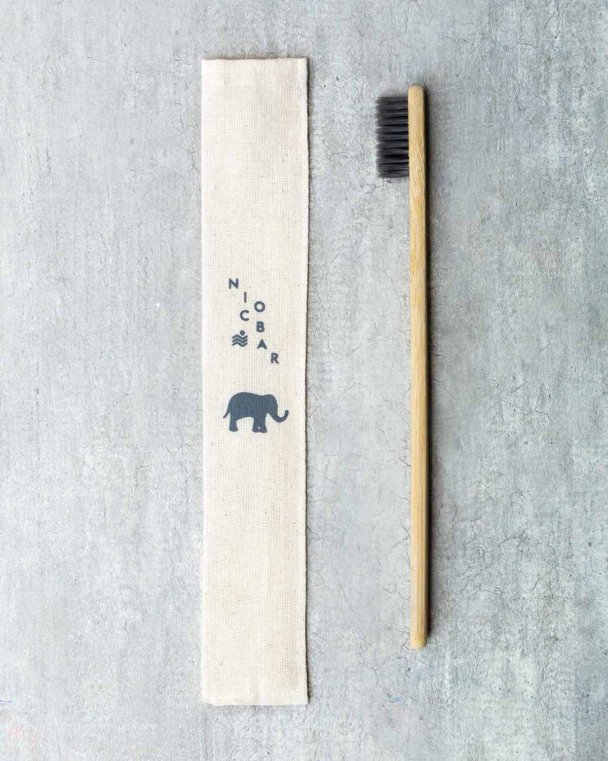 Bamboo Toothbrush with charcoal bristles beside a cotton pouch printed with an elephant.