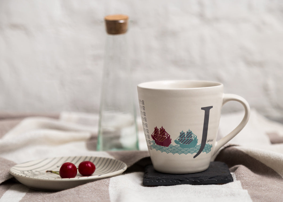 Alphabet J Mug on a slate coaster, showing the two ships and the large J.