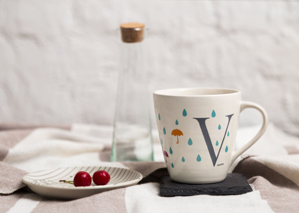 Alphabet V Mug on a table, showing the letter V and raindrop motifs.