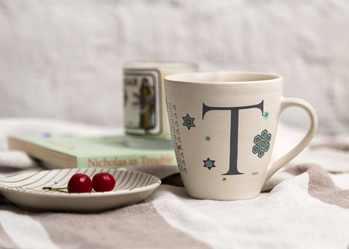 Alphabet T Mug with a large T and star motifs, shown on a table.
