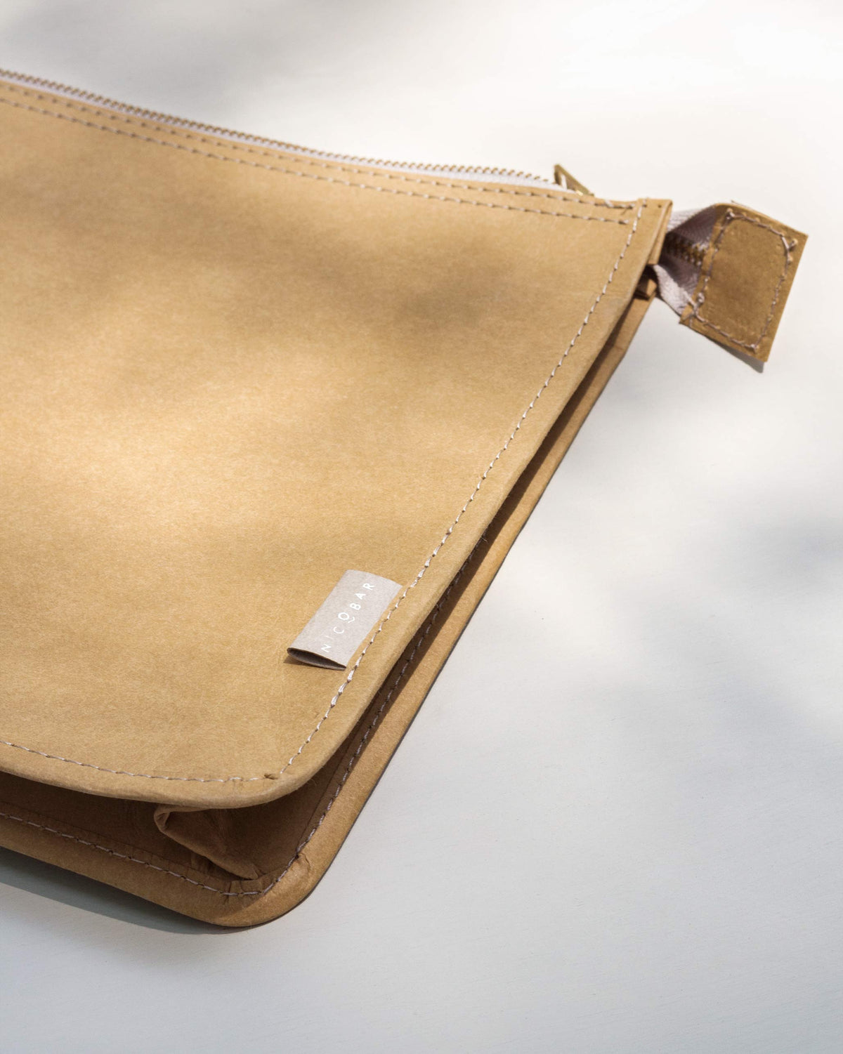 Close-up of a brown Paper Pouch showing its stitched corner and tag.