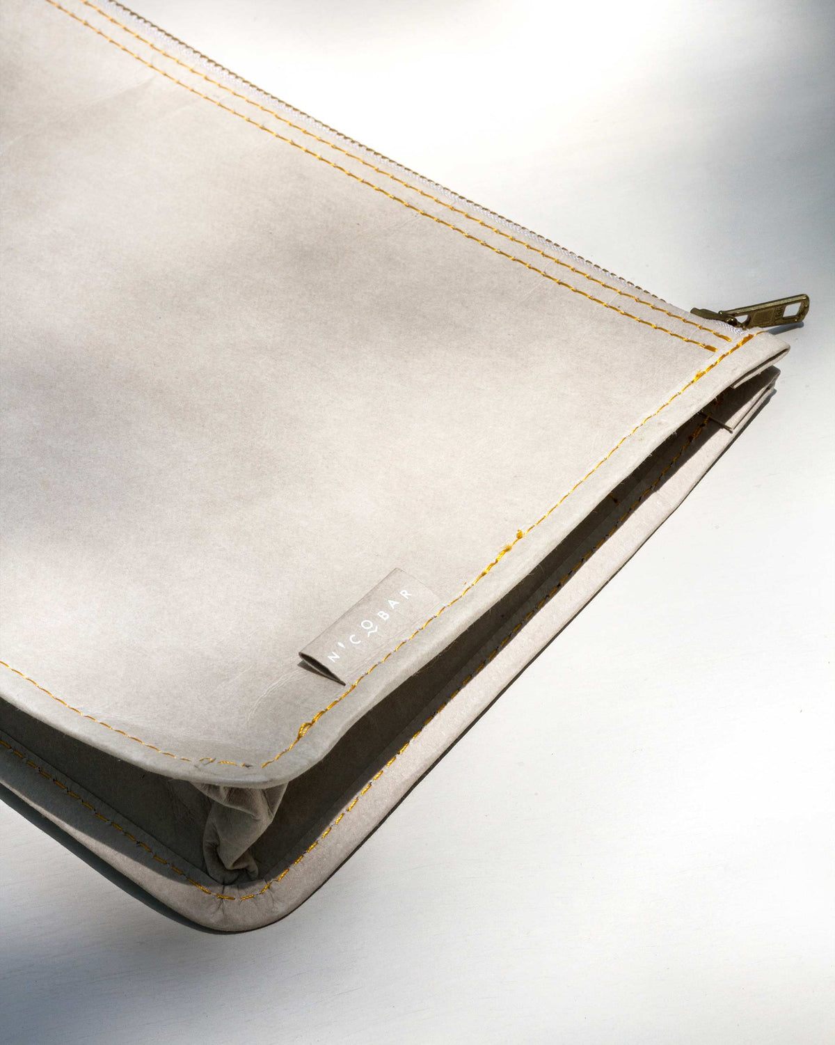 Close-up of a grey Paper Pouch showing gold stitching and a Nicobar tag.