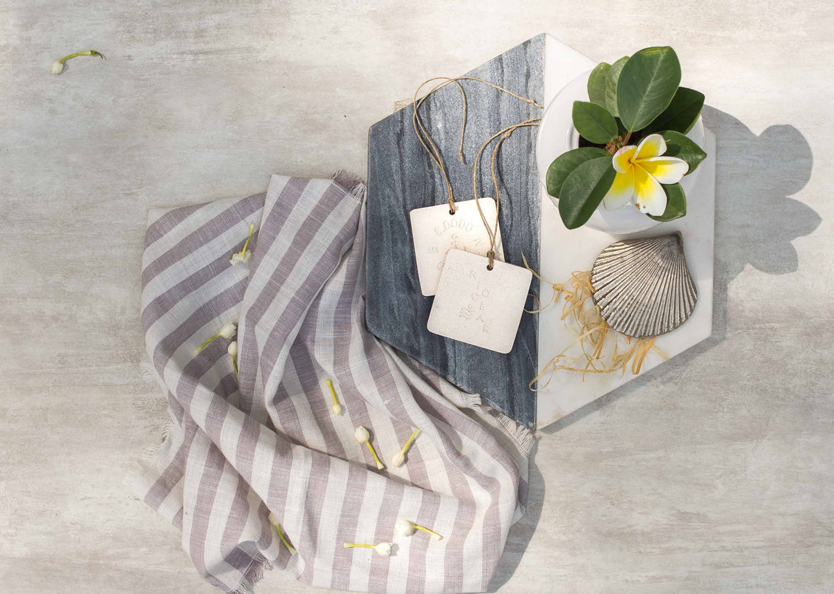 A pair of 2737 BC Ceramic Tiles hung on twine over a striped cloth.