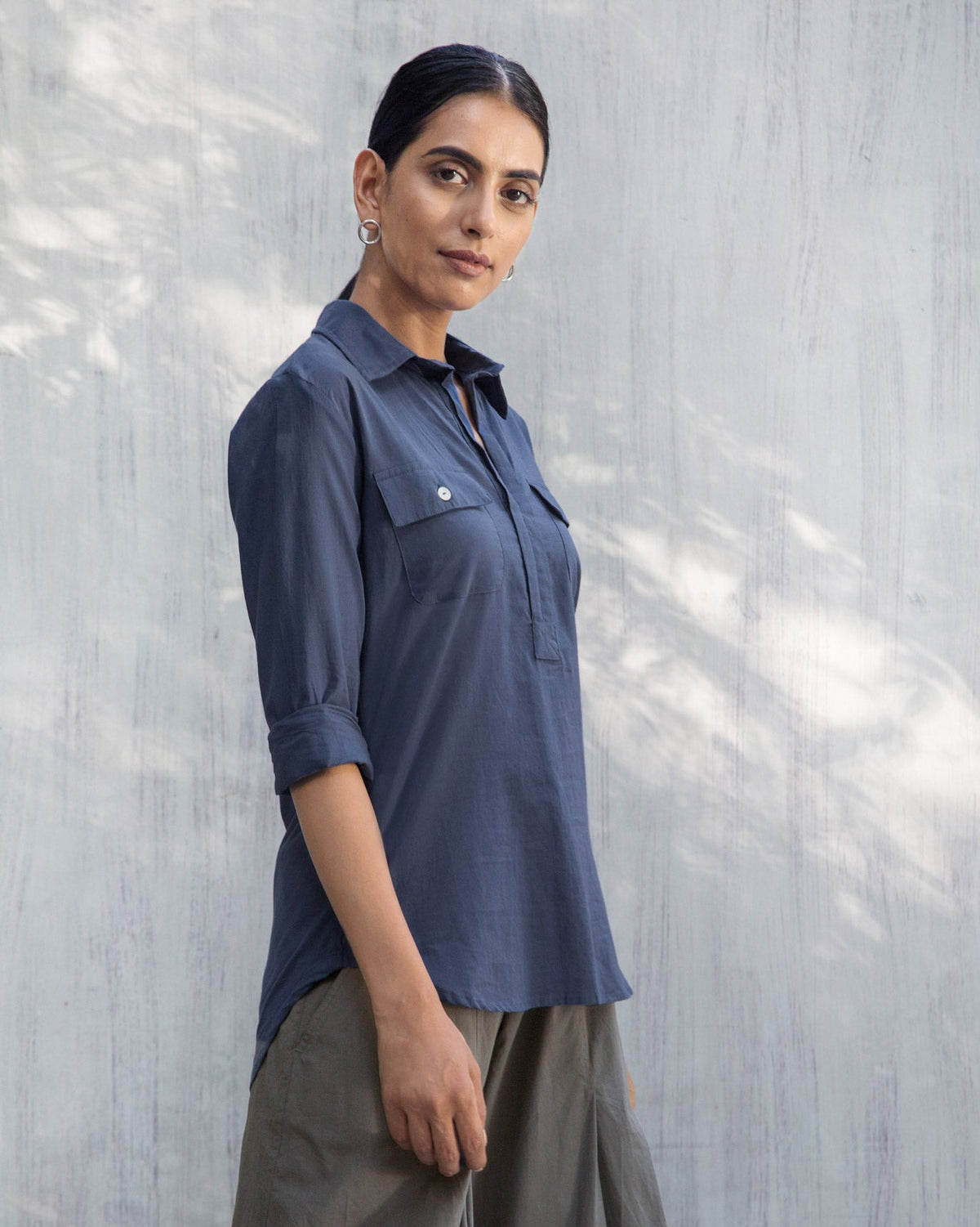 Side view of an indigo Open Collar Top with a curved hem, worn by a person.