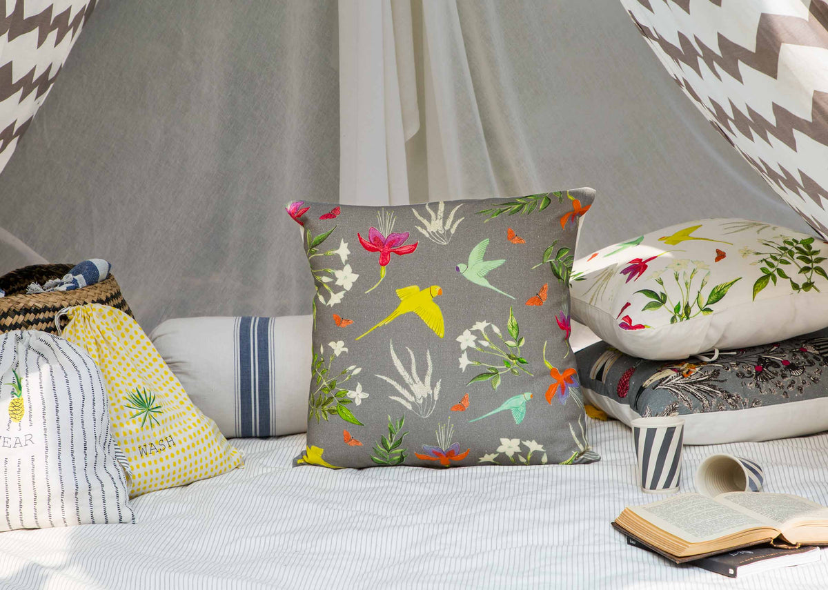 Botanical Cushion Cover on a bed, showing birds and flowers on grey.