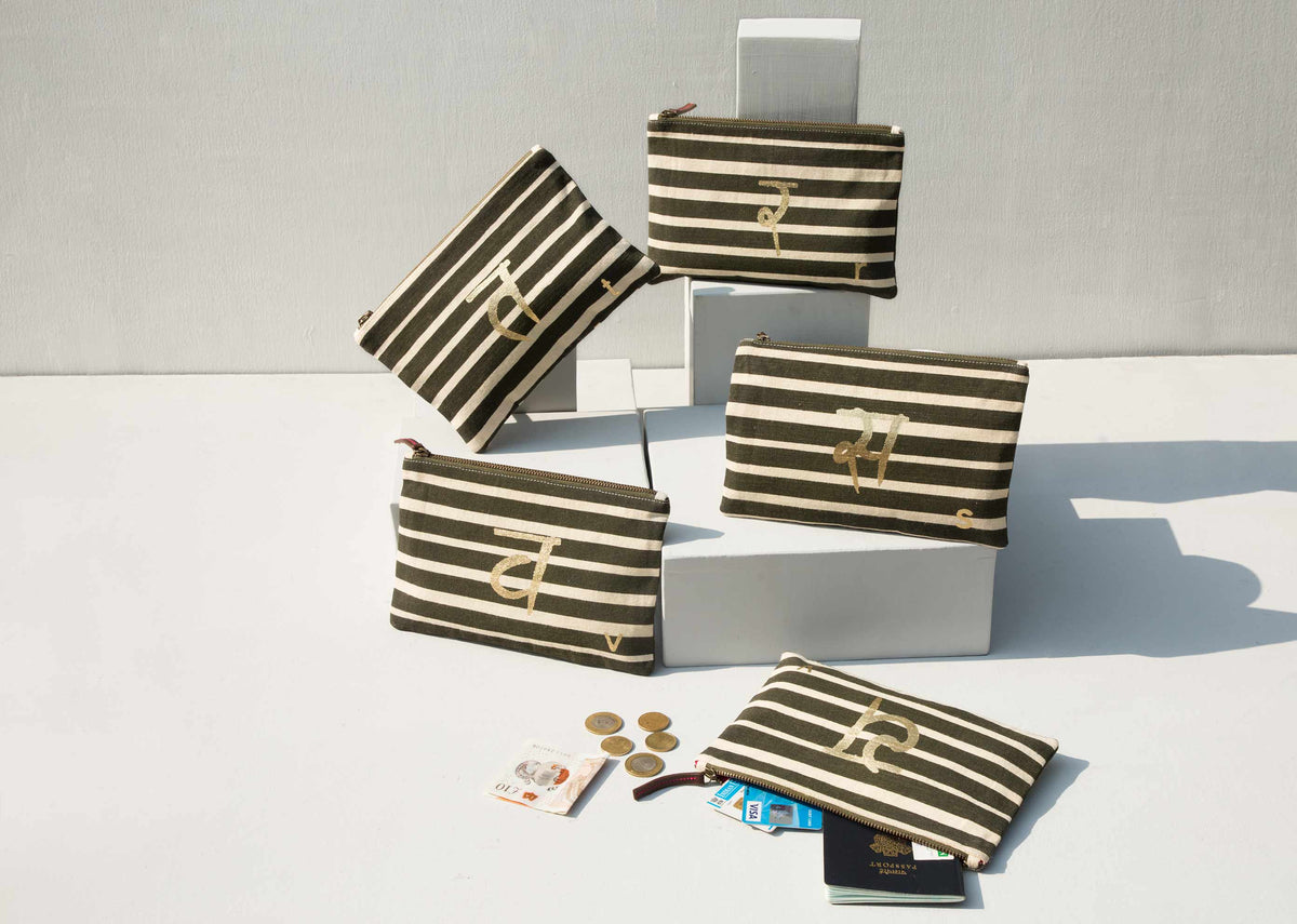 Several olive and cream striped Alphabet pouches with gold letter motifs displayed together.
