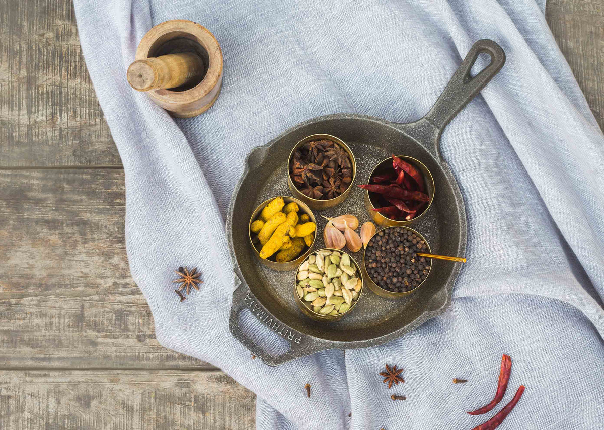 Cast Iron Skillet with small bowls of spices arranged in its pan, seen from above.
