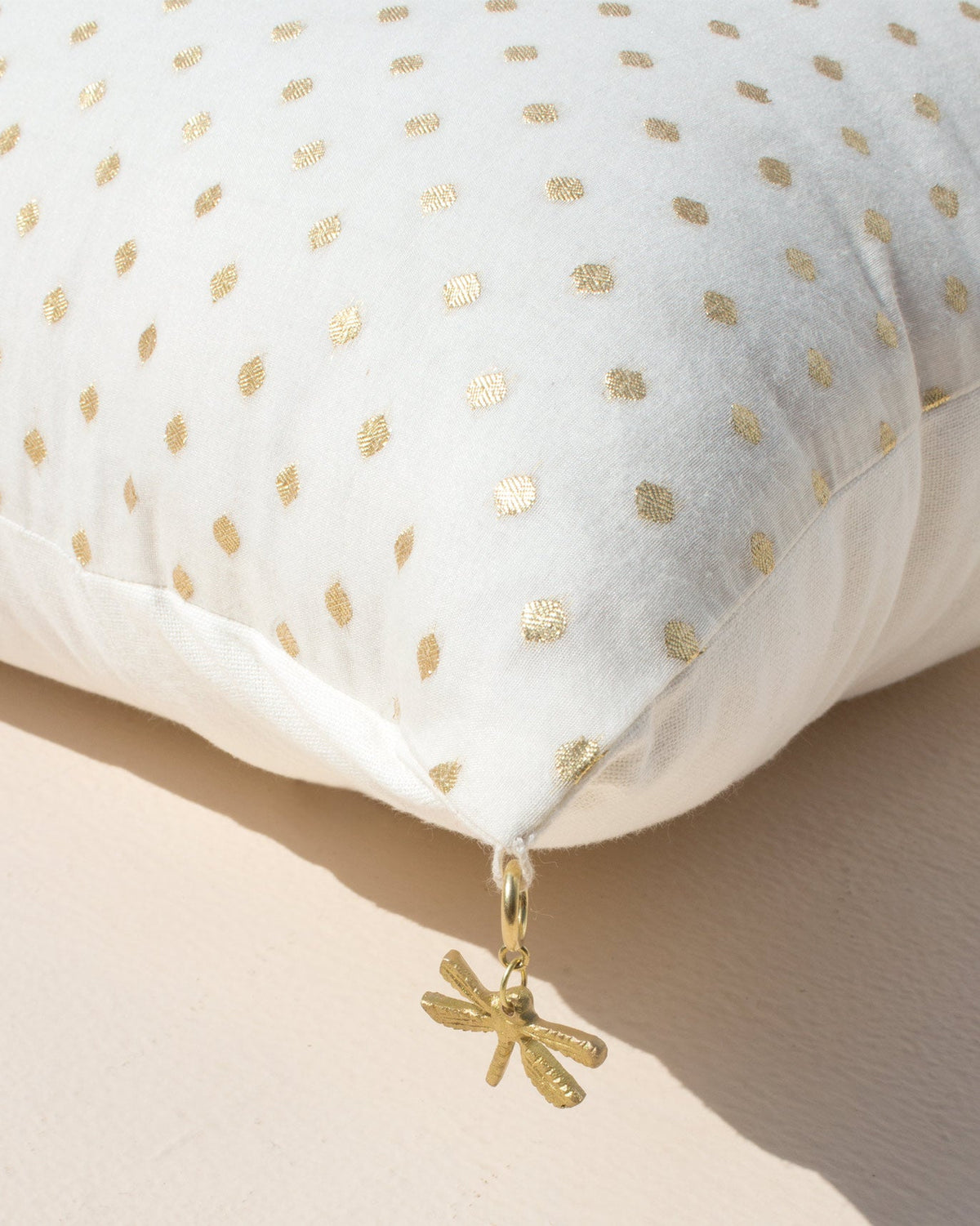Close-up of the Dot Cushion Cover's corner with a small gold charm hanging from it.