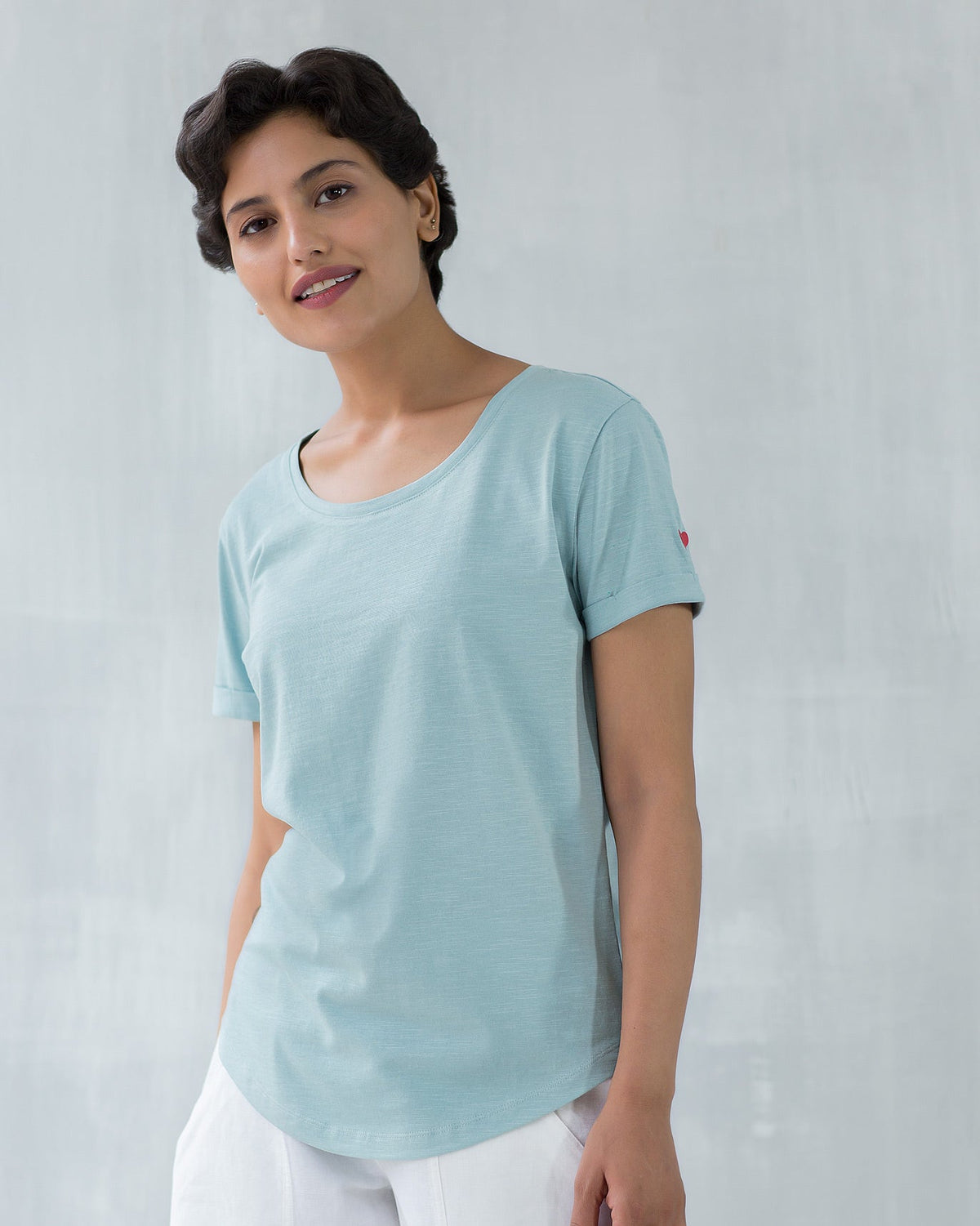 Person wearing a pale blue Basic T-shirt with a small red heart on the sleeve.