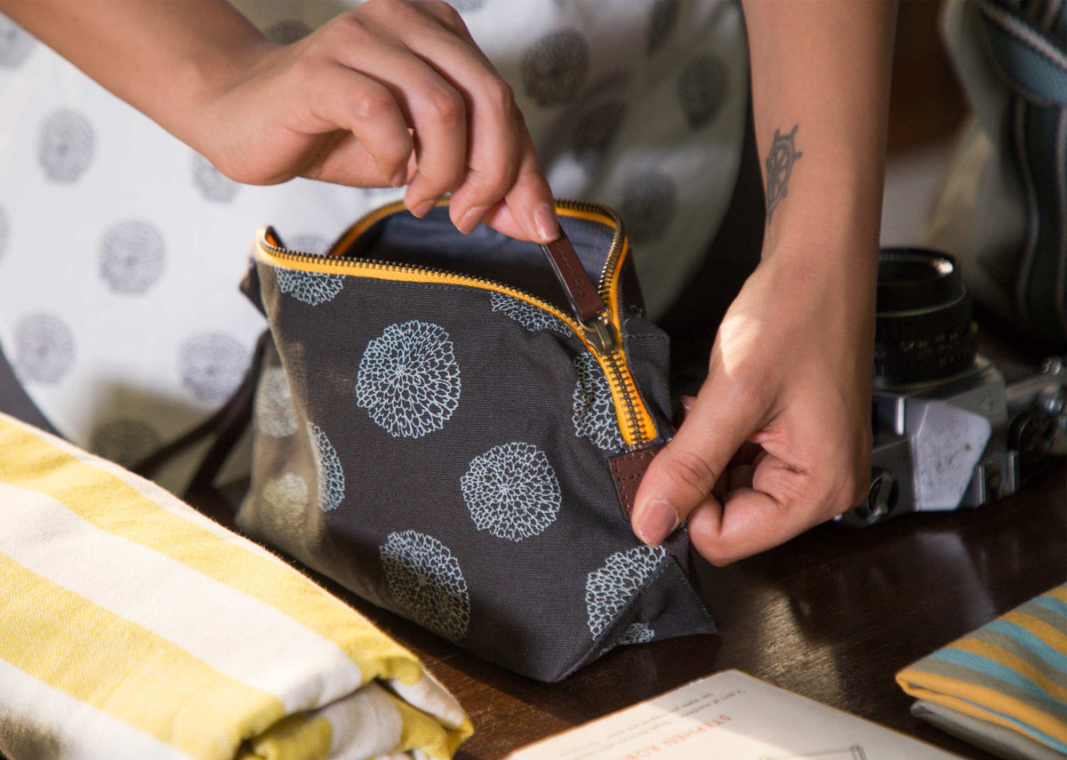 Person opening Marigold Make-Up Pouch by its yellow zip.