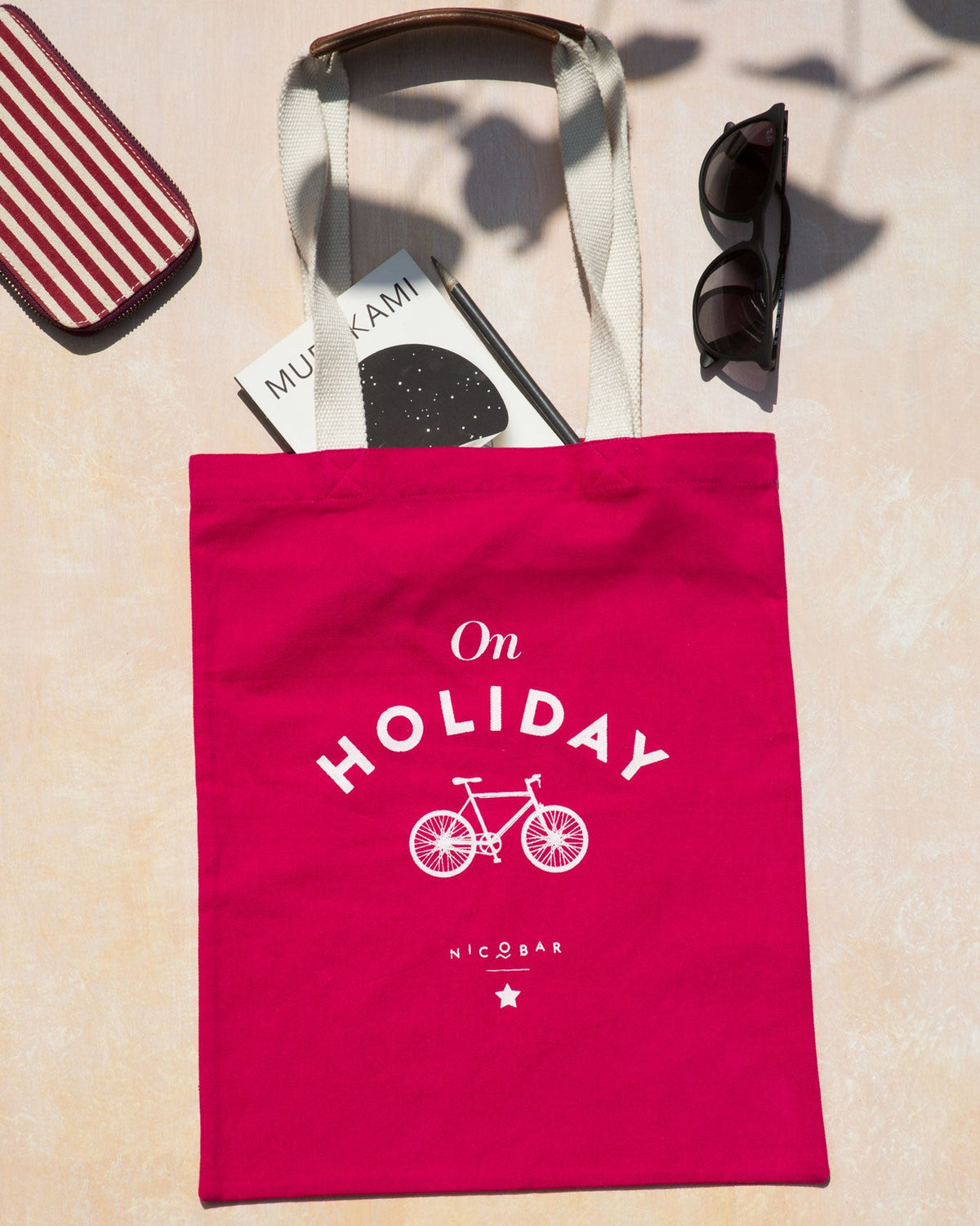 On Holiday tote in pink laid flat, with its cream handles folded up.