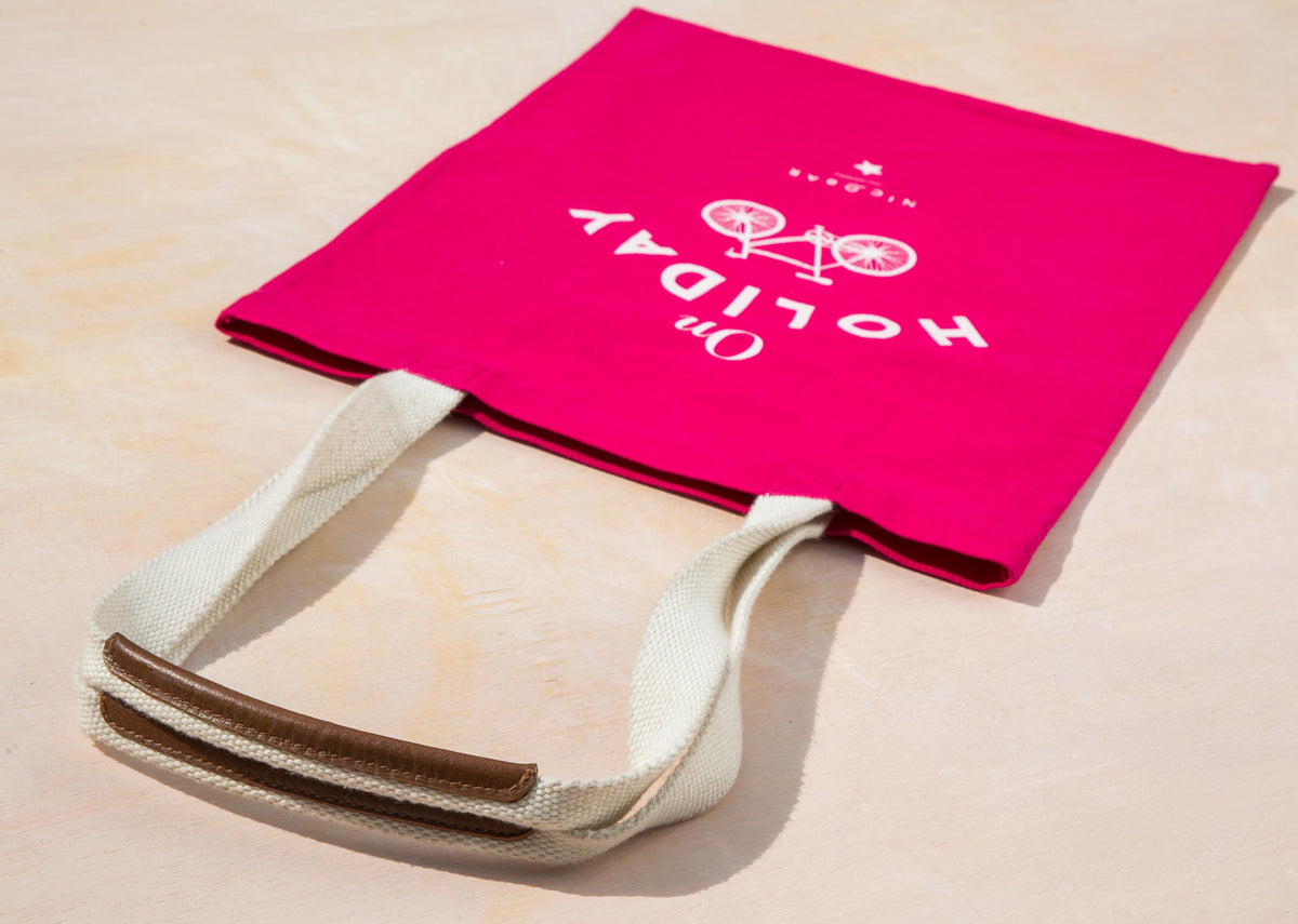 Pink On Holiday tote lying at an angle, showing its leather-tipped handles.